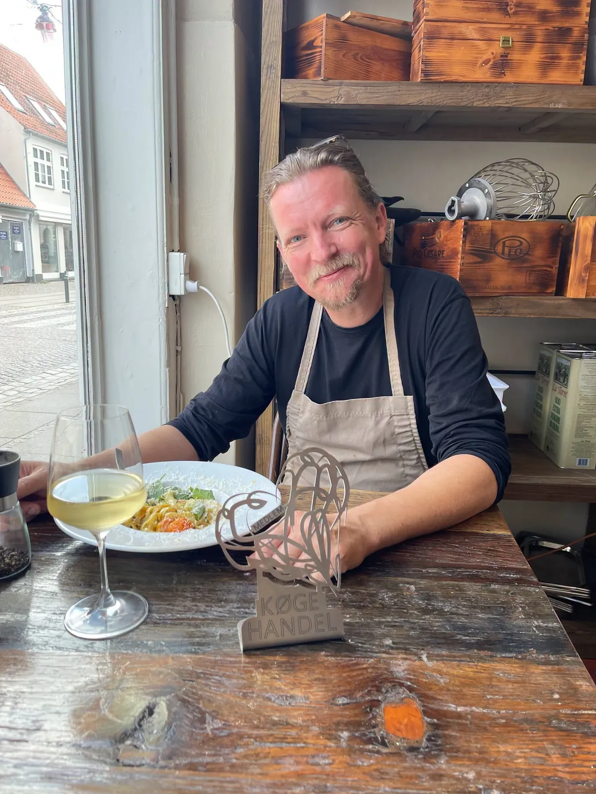 Theis fra Gancio ved vinduesbordet med Køge Handel-medlemsskiltet, en pastaret og et glas hvidvin